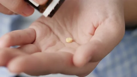Two small yellow round pills fall into palm of hand from pill bottle. Close-up Stockbeeldmateriaal 147189923