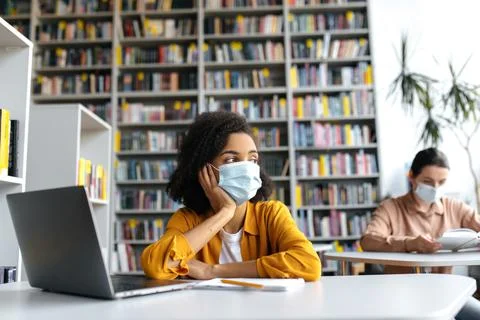 Two smart female students of different nationalities in medical masks are Stock Photos