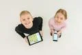 The two smile children stand with devices. View from above Photo