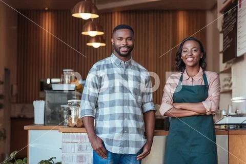 Two smiling African entrepreneurs standing at their cafe counter Stock Photos