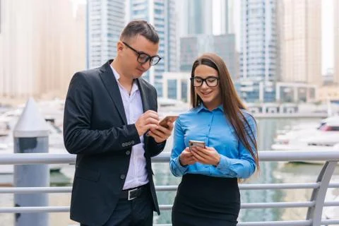 Two smiling business man and woman with mobile phone in hands are having plea Stock Photos