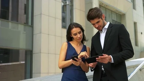 Two smiling business partners using mobile phone and tablet in the street Stock Footage 73813156