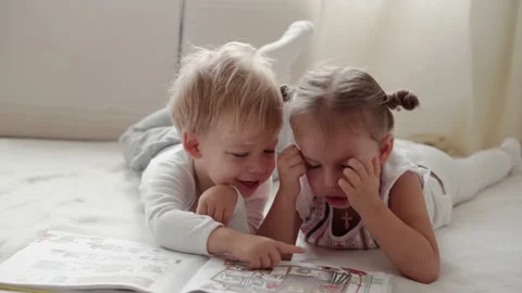 Two smiling children read large interesting book of fairy tales on bed Stock Footage 141175473
