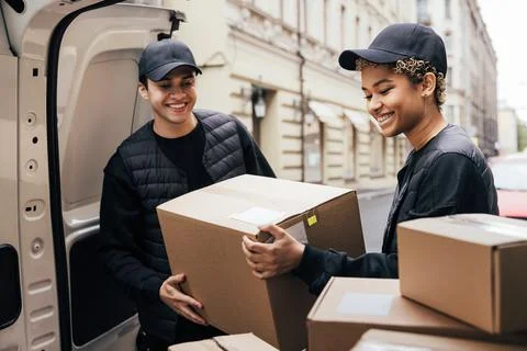 Two smiling couriers unloading cardboard boxes from van in the city Foto stock