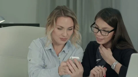 Two smiling coworkers looking at their photos on the phone Stock-Footage 71129028