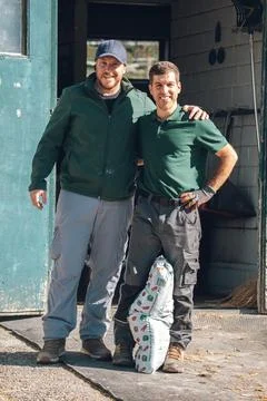 Two smiling farm workers standing outdoors with a bag of produce, showing Фото