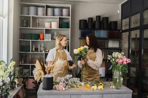 Two smiling florists in uniform work in a flower shop behind counter with 스톡 사진