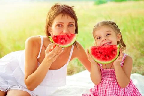 Two smiling girls eats slice of watermelon outdoors on meadow. Mother and Stock Photos