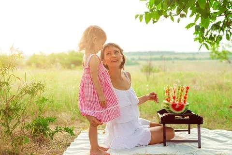 Two smiling girls eats slice of watermelon outdoors on meadow. Mother and Stock Photos