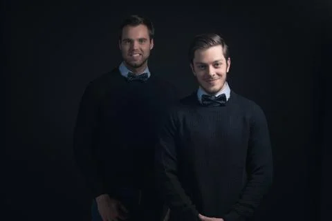 Two smiling men in dark blue sweater with shirt and bow tie. Stock Photos