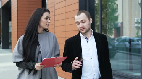 Two smiling smart partners walk on the city street and discussing about new conc Stock Footage 199491998
