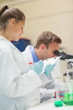 Two smiling students looking through microscope and taking notes 스톡 사진