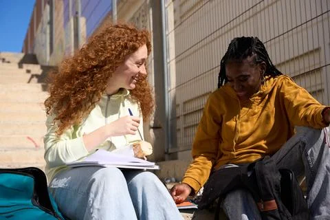 Two smiling students studying and eating together outdoors Stock Photos