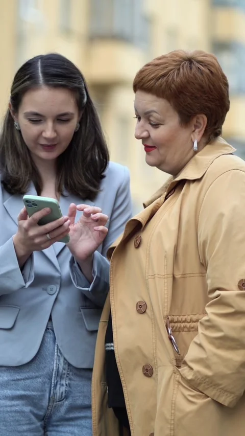 Two smiling women of different generations chat outdoors on a city street Stock Footage 341903113