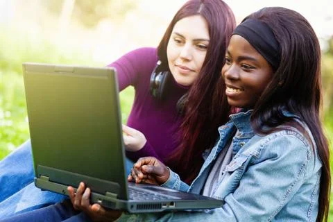 Two smiling young girls using laptop at the park. Stock Photos