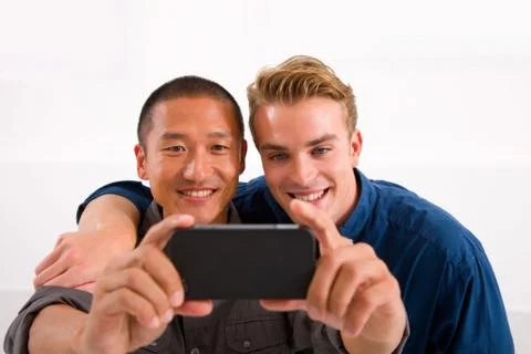 Two smiling young men taking self portrait with cell phone Stock Photos