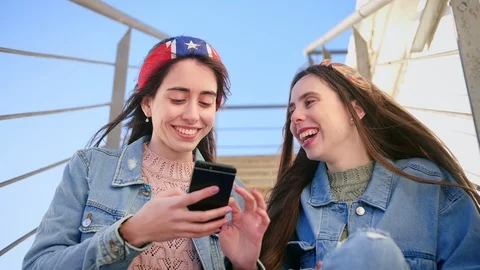 Two smiling young sisters use new application on smart phone device, watching on Stock Footage 106194773