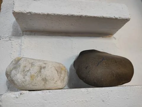 Two smooth rocks on the white wall, one is slightly larger than the other a.. Stock Photos