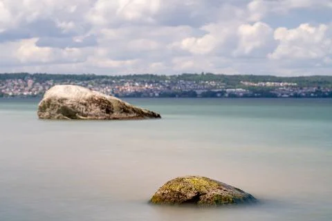 Two smooth, weathered rocks emerge from the calm water Stock Photos