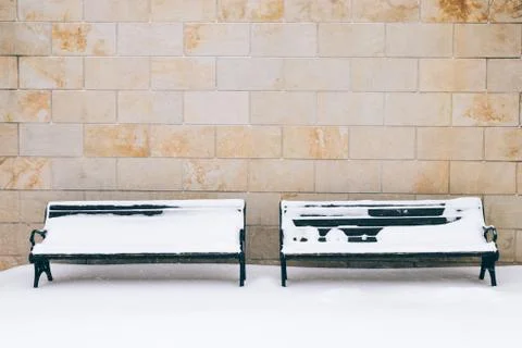 Two snow-covered bench against a brick wall in winter Stock Photos