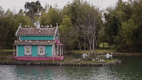 Two snow-white swans are swimming on the swan lake near the colorful bird house 動画素材 113996946