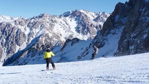 Two snowboarders riding down the slope at moutain ski resort Shymbulak. Tourism Stock-Footage 332873933