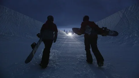 Two snowboarders walk through a half pipe at night Stock Footage 116786227
