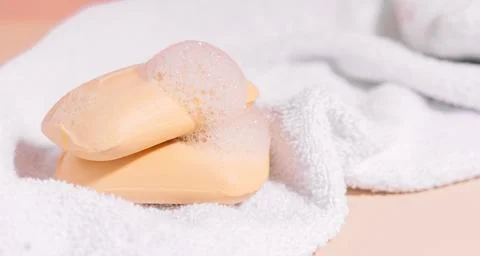 Two soap bars of soap on a white towel on a beige background Stock Photos