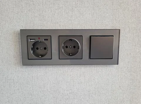 Two sockets and a switch that provide access to electricity on the wall Stock Photos