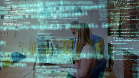 Two software developers collaborating at desk in open-plan office, with floating Stock Footage 308572237