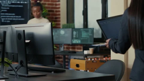 Two software developers coming at desk and sitting down holding laptop with Stock Footage 168231625