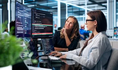 Two Software Developers Compare And Discuss Code Changes On Laptop Screens To Stock Photos
