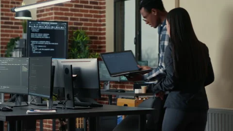 Two software developers holding laptop with coding interface walking towards Stock Footage 168232176