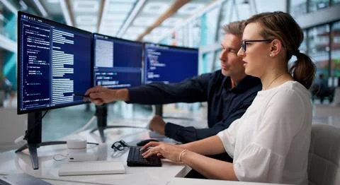 Two Software Engineers Coding Secure Systems Together At Office Desk. Stock Photos