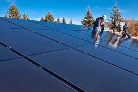 Two solar panel installers install solar panels on roof, Alberta foothills near Stock Photos