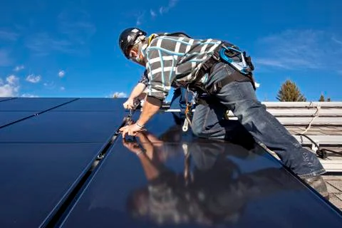 Two solar panel installers install solar panels on roof, Alberta foothills near Stock Photos