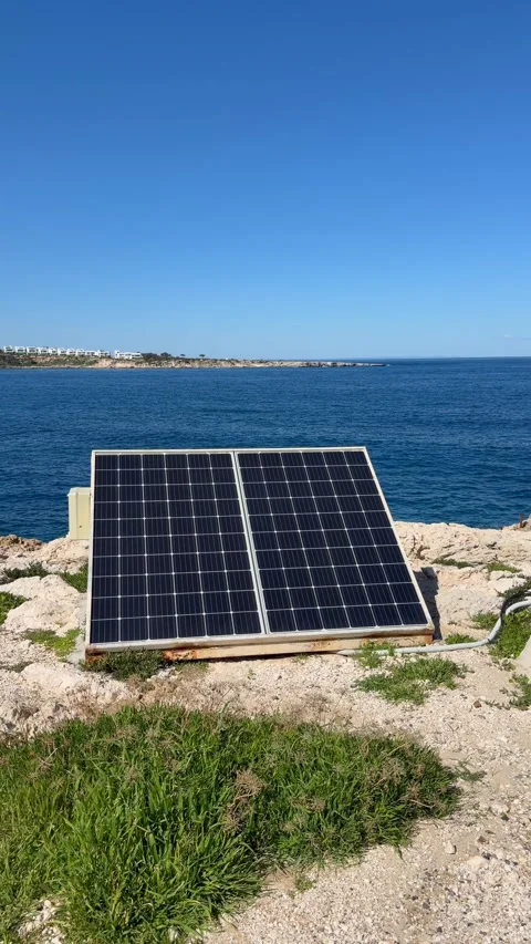 Two solar panels mounted on rocky coastal ground face open blue sea in clean Stock Footage 334577619