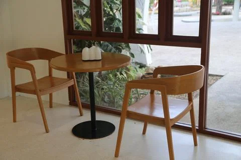 Two solid wood chairs and a round table in front of a window, in a small co.. Stock Photos