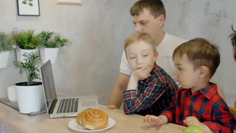 Two sons and father sitting at the kitchen counter with baked roll on a plate Stock Footage 91465722