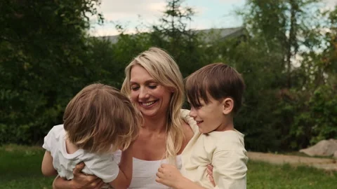 Two sons of different ages hug their mother on the lawn. Stock Footage 217804939