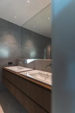Two spacious white bathroom sinks in front of a mirror with gray wall and wood Stock Photos