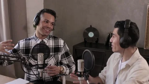 Two speakers discussing and smiling at table in front of microphones and Stock Footage 162228876