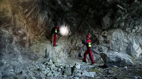 Two speleologists in red suits researchs cave with lantern Stock Footage 76584393