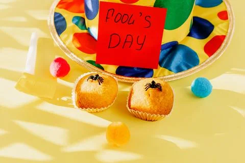 Two spider muffins, a clown hat and an Fool's Day note on yellow. Stock Photos