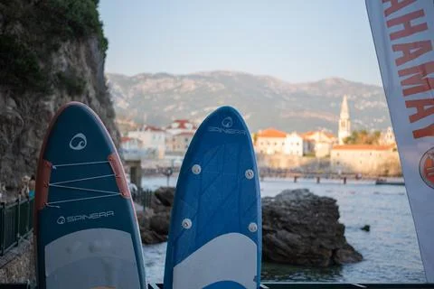 Two Spinera stand-up paddleboards stand upright with coastal bay in background Stock Photos