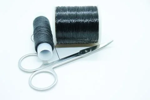 Two spools of black thread and scissors located on a white background Stock Photos
