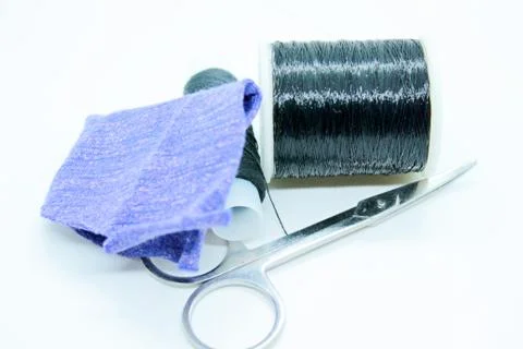 Two spools of black thread, fabric and scissors are located on a white backgr Stock Photos
