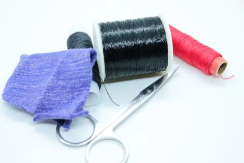 Two spools of black thread, fabric and scissors are located on a white backgr Stock Photos