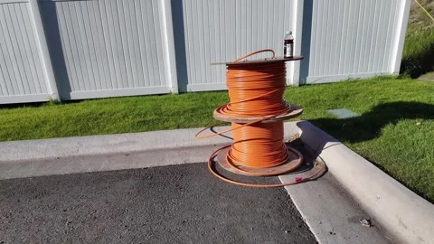 Two spools of industrial orange cable wire along white fence line of a parking 库存影片 340046084