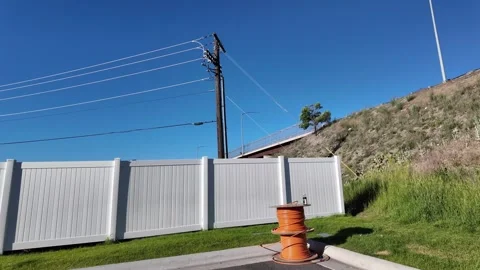 Two spools of industrial orange cable wire along white fence line of a parking 스톡 동영상 340046264